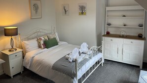 Quarto bem arrumado com cama, abajur e cômoda branca com prateleiras.