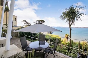 An outdoor patio with a round table and chairs, a large umbrella, and a view of the sea. - 180° Water View Apartment - Simply Amazing (Torquay)