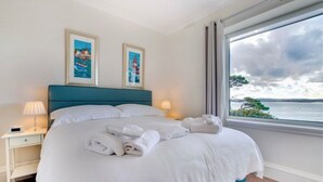 Een hotelkamer met een groot bed, twee ingelijste foto's aan de muur, een nachtkastje met een lamp en een raam met uitzicht op zee.