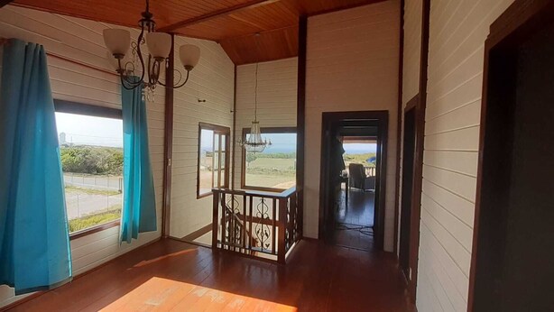 Habitación con piso de madera, un candelabro y vista al exterior, además de una puerta que da a otra habitación.