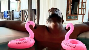 Una persona recostada en una bañera con dos flotadores con forma de flamenco rosa.