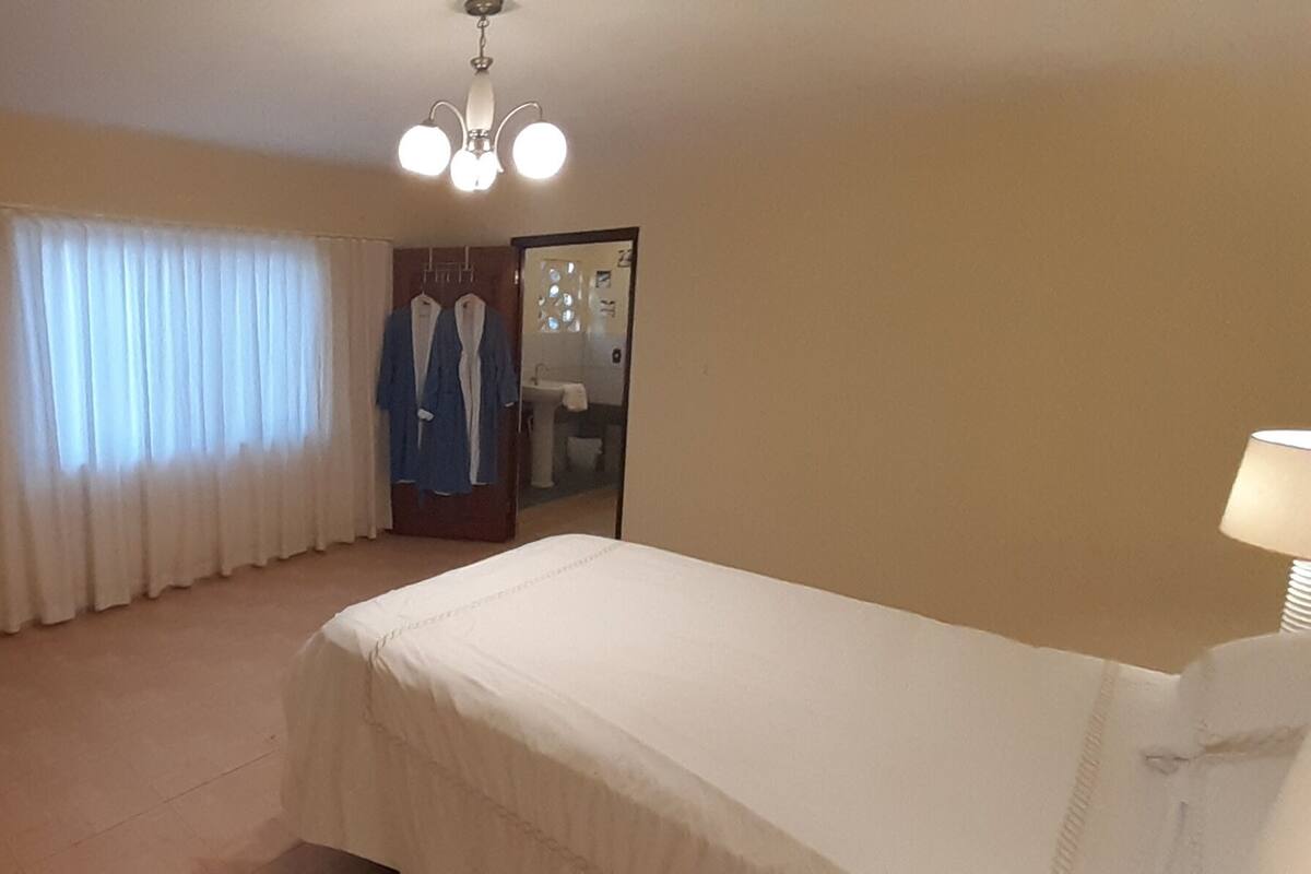 A bedroom with a bed, a door, a window with curtains, a mirror, and a ceiling light fixture.