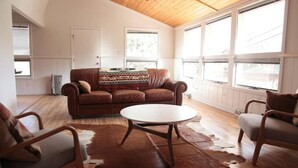 A cozy living room with a brown leather sofa, a round coffee table, and a cowhide rug. - Magnolia Mountain Getaway (Nederland)