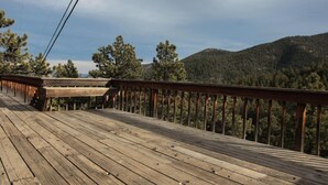 A wooden deck with a railing overlooking a forested mountain area. - Magnolia Mountain Getaway (Nederland)
