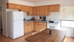 A kitchen with wooden cabinets, a white refrigerator, a stove, and a dining table. - Magnolia Mountain Getaway (Nederland)