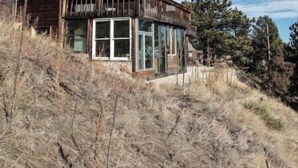A two-story wooden house with large windows and a balcony, surrounded by dry grass and trees. - Magnolia Mountain Getaway (Nederland)