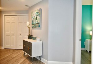 A hallway with a white console table, a painting, and a white door.