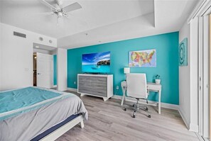 A bedroom with a bed, a desk, a chair, a TV, and artwork on the walls.
