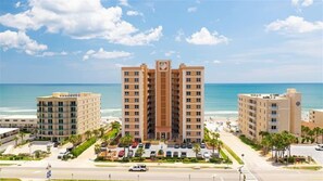 A beachfront hotel with multiple buildings, a parking lot, and a clear view of the ocean.