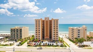 Un hotel frente a la playa con varias edificaciones, un estacionamiento y vista despejada al océano.