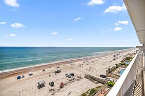 Vista a la playa desde un balcón con una playa arenosa, vehículos y zona de piscina.