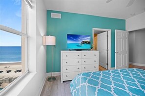 A bedroom with a large window, a bed with a patterned bedspread, a dresser, and a television on top.