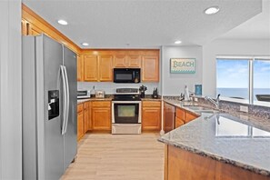 Una cocina moderna con armarios de madera, electrodomésticos de acero inoxidable y un amplio ventanal con vistas a la playa.