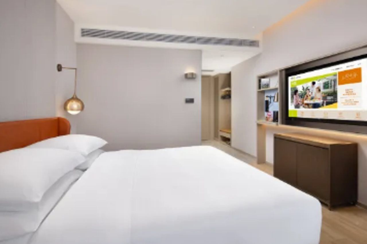 A modern hotel room with a large bed, a flat-screen TV, and a wooden cabinet.