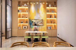A modern dining area with a central table, surrounded by chairs, and flanked by illuminated shelves with books and decorative items. - Home2 Suites By Hilton Shenzhen Dalang (Shenzhen)