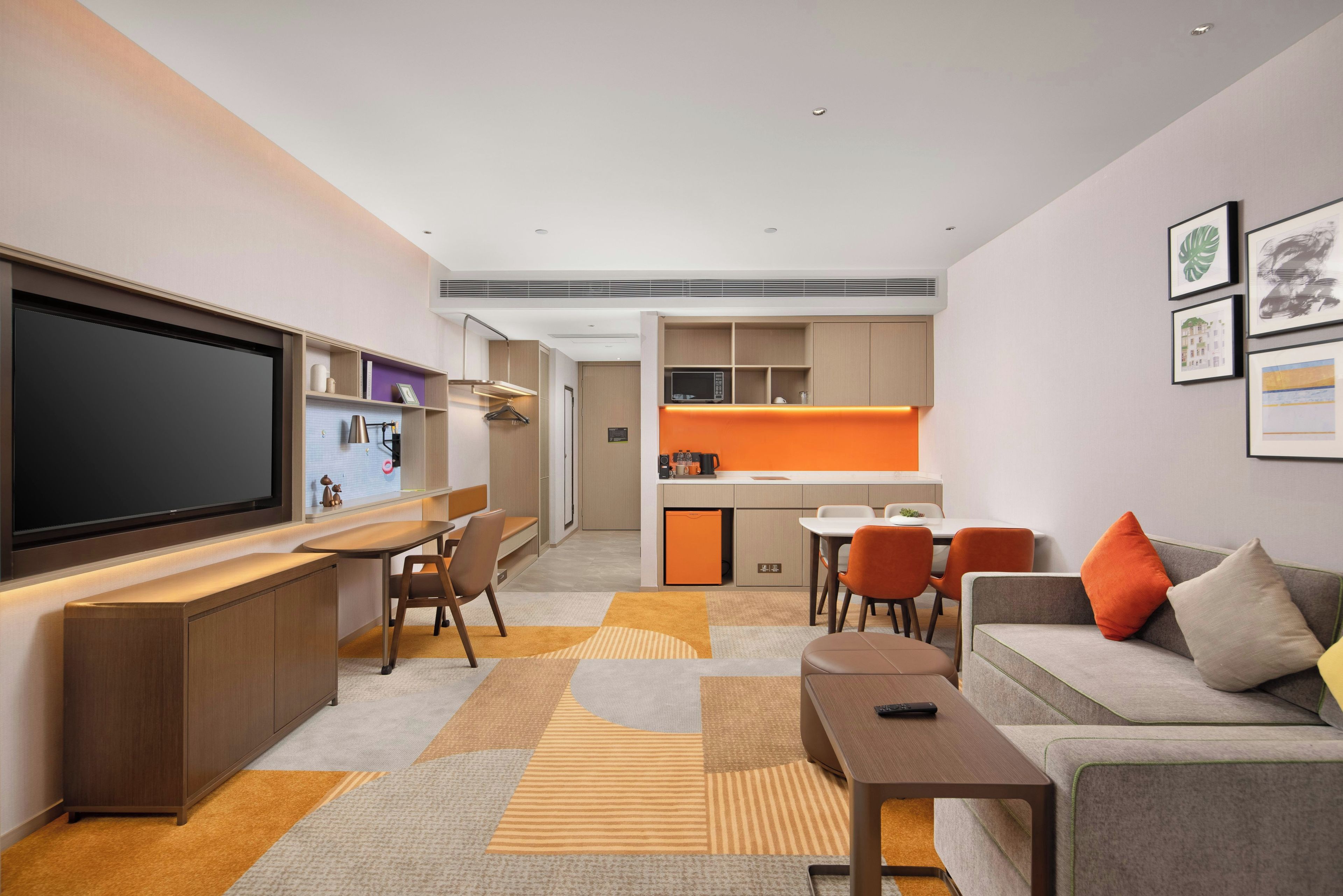 A modern living room with a flat-screen TV, seating area, and a kitchenette in the background.