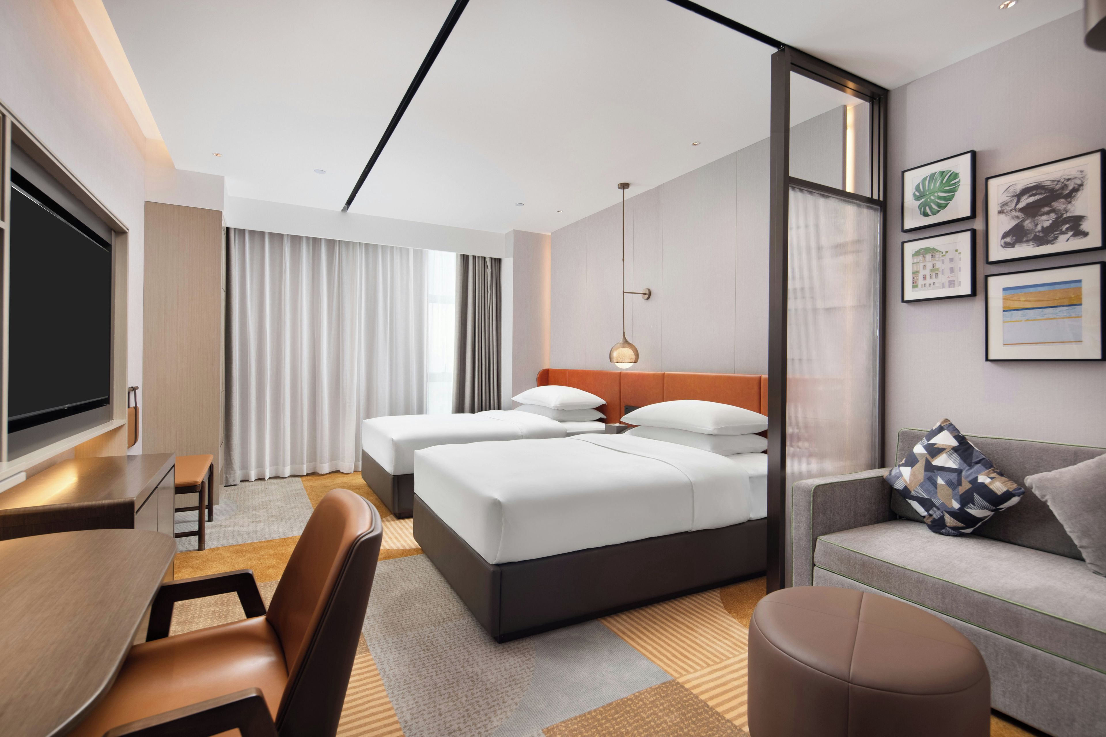 Ein Hotelzimmer mit Bett, Schreibtisch, Fernseher, Sofa und einer Wand mit gerahmten Bildern.