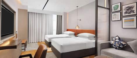 A hotel room with a bed, a desk, a TV, a sofa, and a wall with framed pictures.