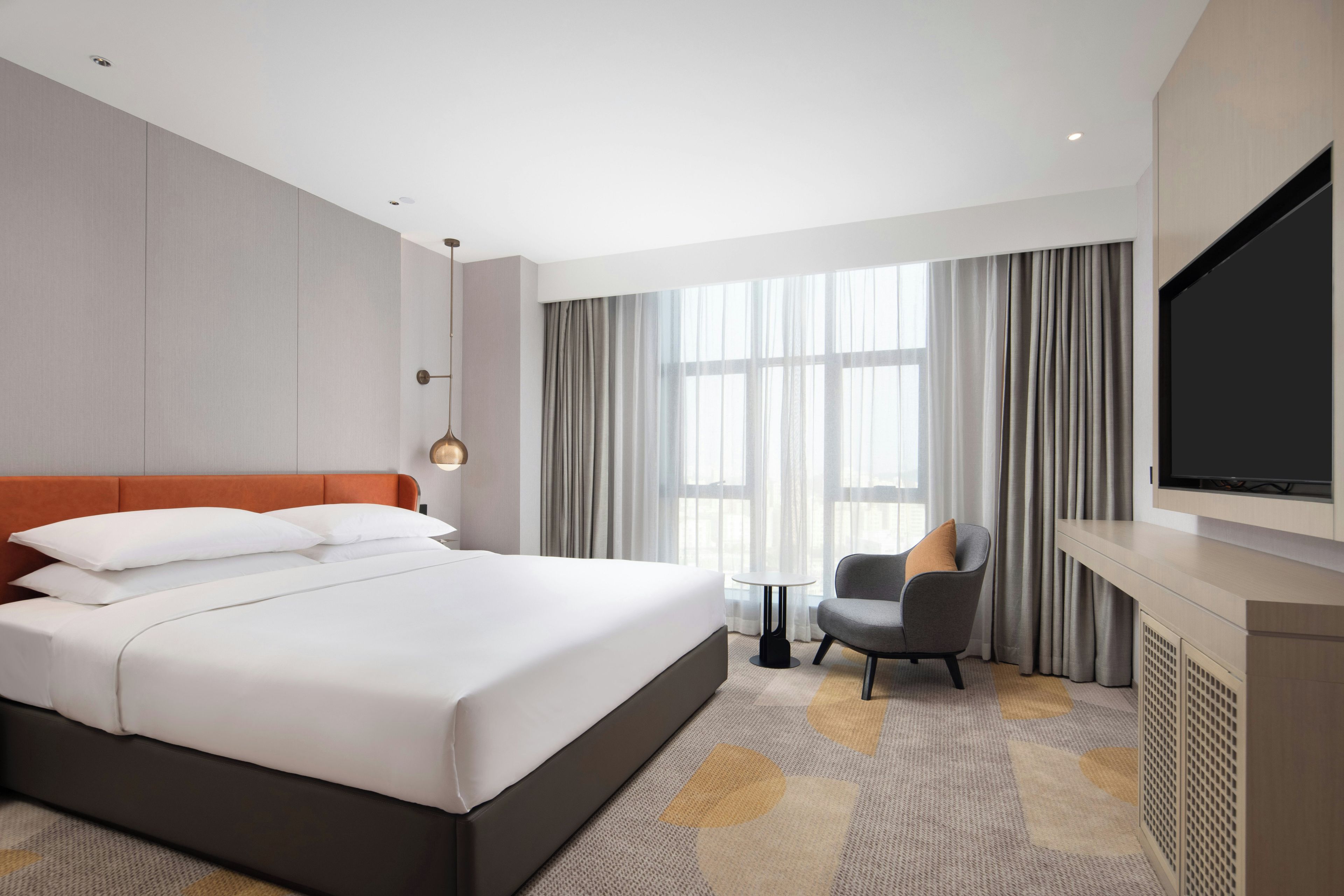 A hotel room with a large bed, a television, a chair, and a window with curtains.