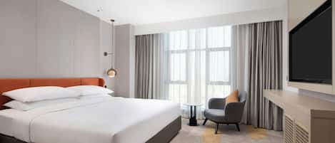 A hotel room with a large bed, a television, a chair, and a window with curtains.