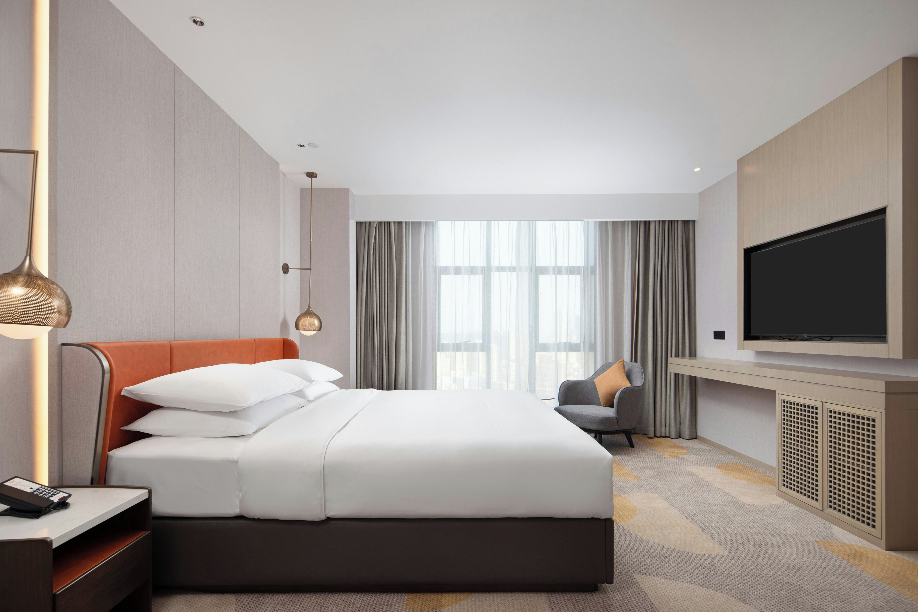 A hotel room with a large bed, a television, a desk with a lamp, and a view of the city through the window.