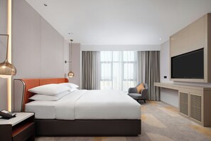 A hotel room with a large bed, a television, a desk with a lamp, and a view of the city through the window. - Home2 Suites By Hilton Shenzhen Dalang (Shenzhen)