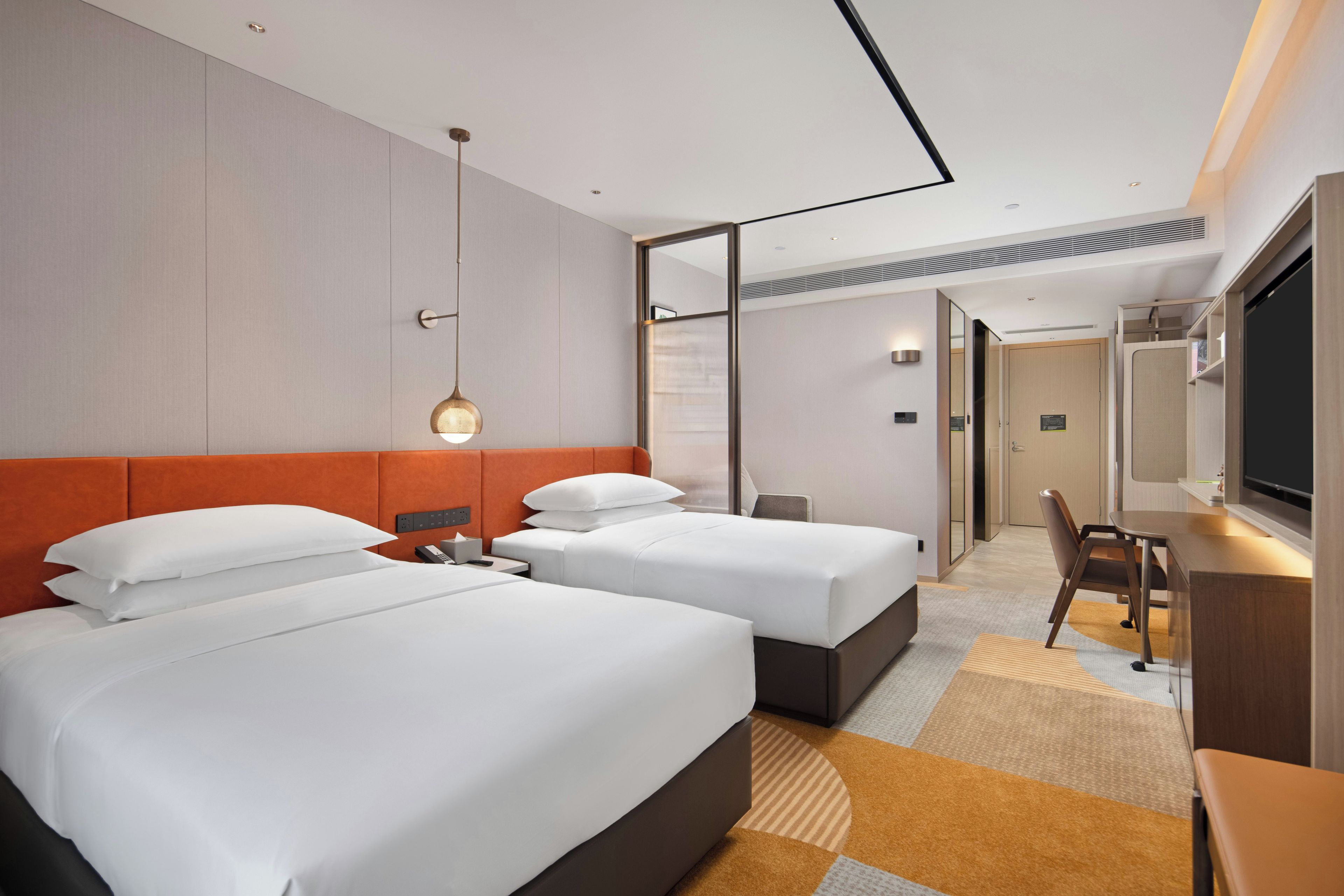 A hotel room with two beds, a desk, a chair, and a television.