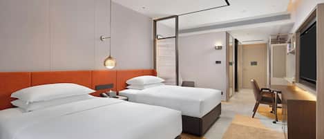 A hotel room with two beds, a desk, a chair, and a television.