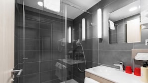 Un baño moderno con ducha cubierta por vidrio, un lavamanos blanco y un espejo encima.