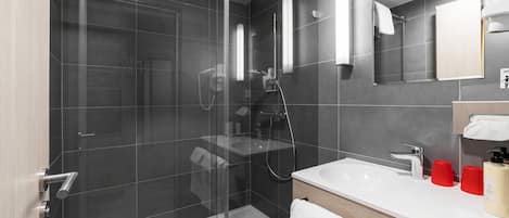 Un baño moderno con ducha cubierta por vidrio, un lavamanos blanco y un espejo encima.