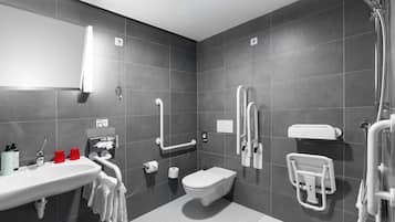 A modern bathroom with a sink, toilet, and shower. It includes grab bars and a hand dryer.