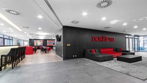 Un espacio de oficina moderno con una pared negra que muestra el nombre 'DORNER' en letras rojas, suelo de baldosas grises y un sofá rojo y negro.