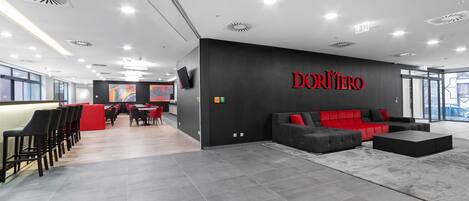 Un espacio de oficina moderno con una pared negra que muestra el nombre 'DORNER' en letras rojas, suelo de baldosas grises y un sofá rojo y negro.