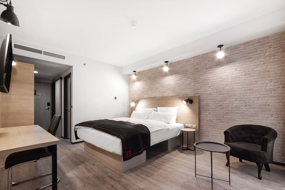 A modern hotel room with a bed, a desk, a chair, and a small table.