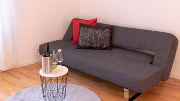 Ein modernes Wohnzimmer mit einem grauen Sofa, roten und schwarzen Kissen, einem runden Couchtisch mit Vase und Flasche sowie einer Wandsticker mit einem Hirschmotiv.