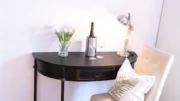 A room with a black table, a white chair, a vase with flowers, a bottle, and a lamp.