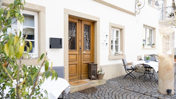 A cobblestone courtyard with a wooden door, a table with chairs, and a potted plant. - Cabinett 1876 (Trittenheim)