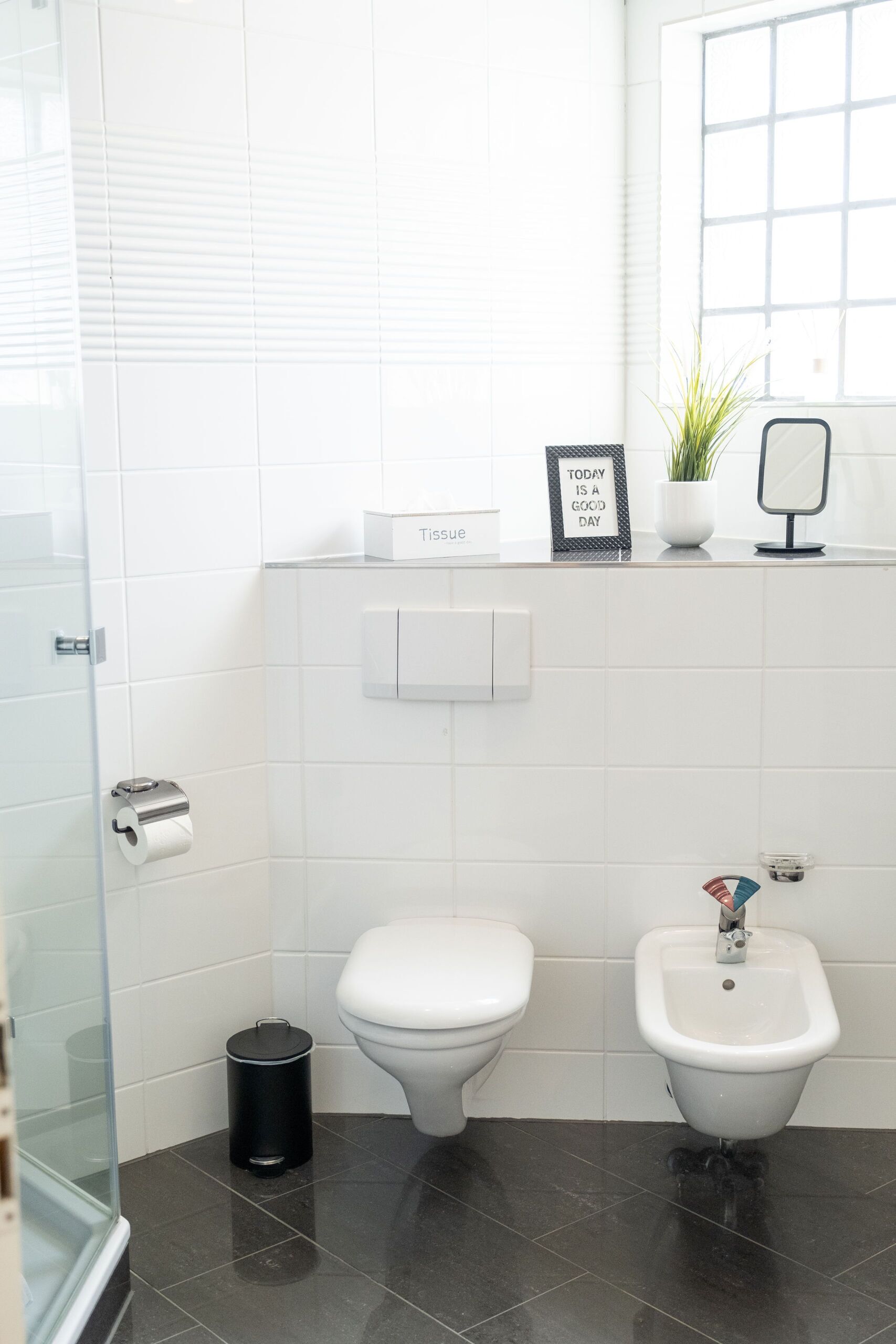 Un baño moderno con inodoro, bidé y cubo de basura.