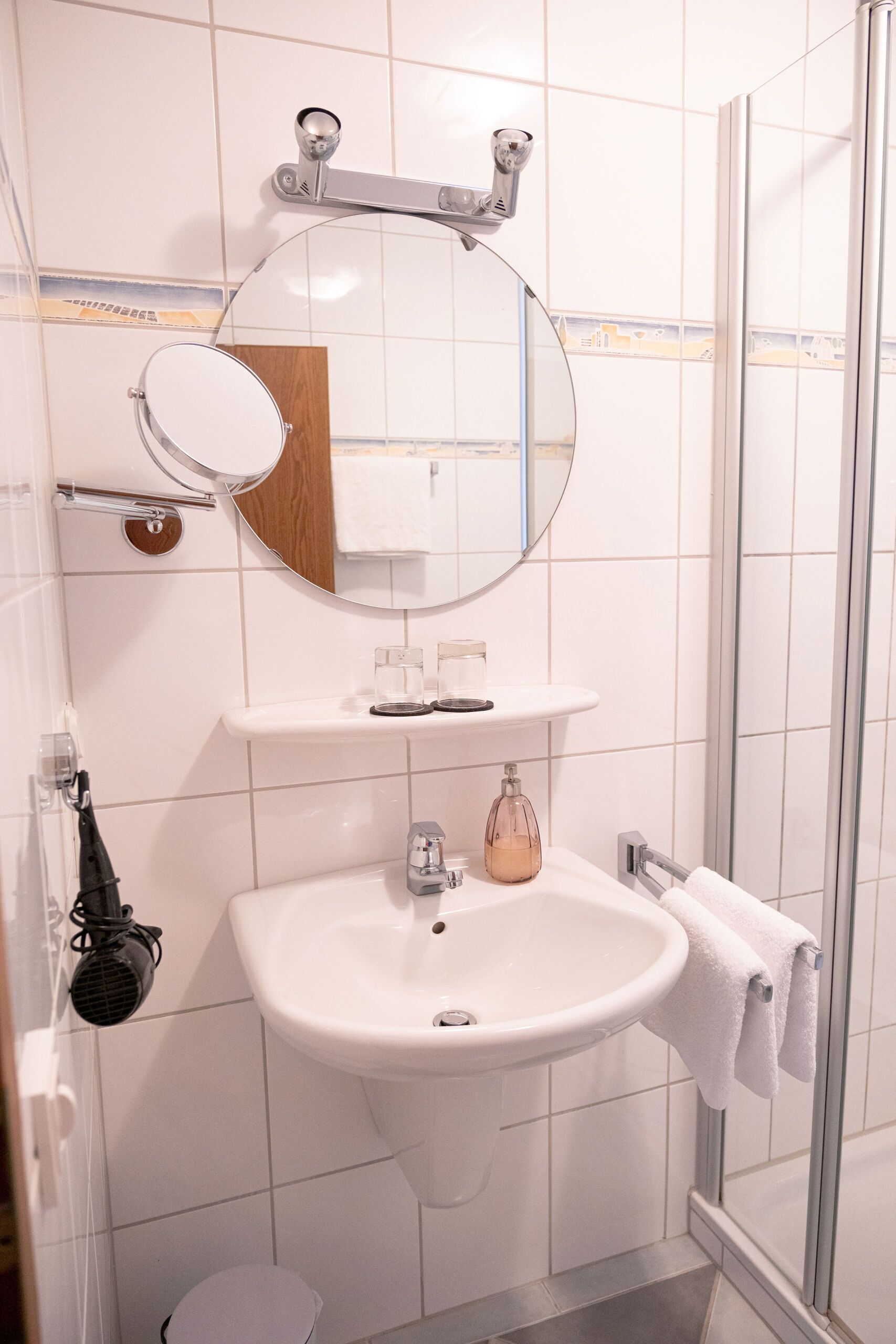 Une salle de bain avec un lavabo blanc, un miroir, un porte-serviettes et une cabine de douche en verre.