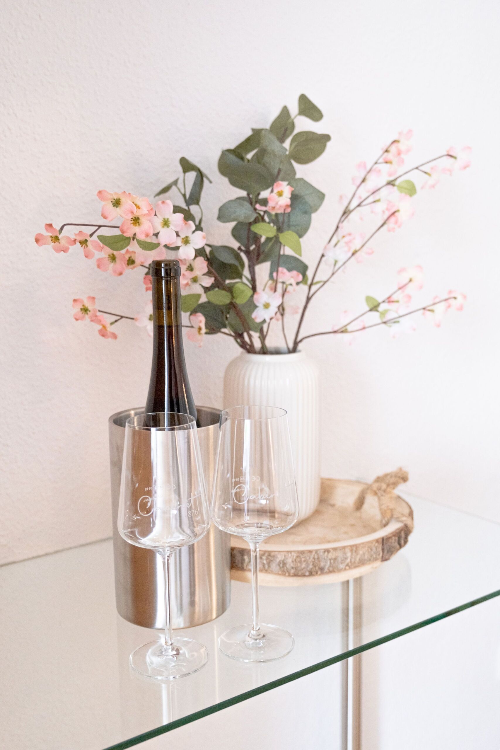Eine Flasche Champagner in einem silbernen Kübel mit zwei Gläsern auf einem Glastisch.
