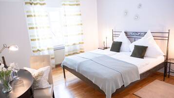 A neatly arranged bedroom with a bed, bedside tables, a chair, and a table with a vase of flowers.