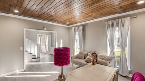 A spacious living room with a high wooden ceiling, a beige sofa, a coffee table, and a pink lamp. - Royal Meadows (Jackson)