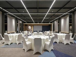 A conference room with round tables, white chairs, and a large screen at the front. - ibis Surabaya Tidar (Surabaya)