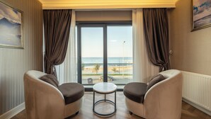 Una habitació amb dos sofàs i una taula petita, un finestral gran amb cortines i vista a la platja.
