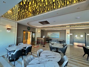 A modern dining area with marble tables and leather chairs, a ceiling with star decorations, and a painting of mountains.