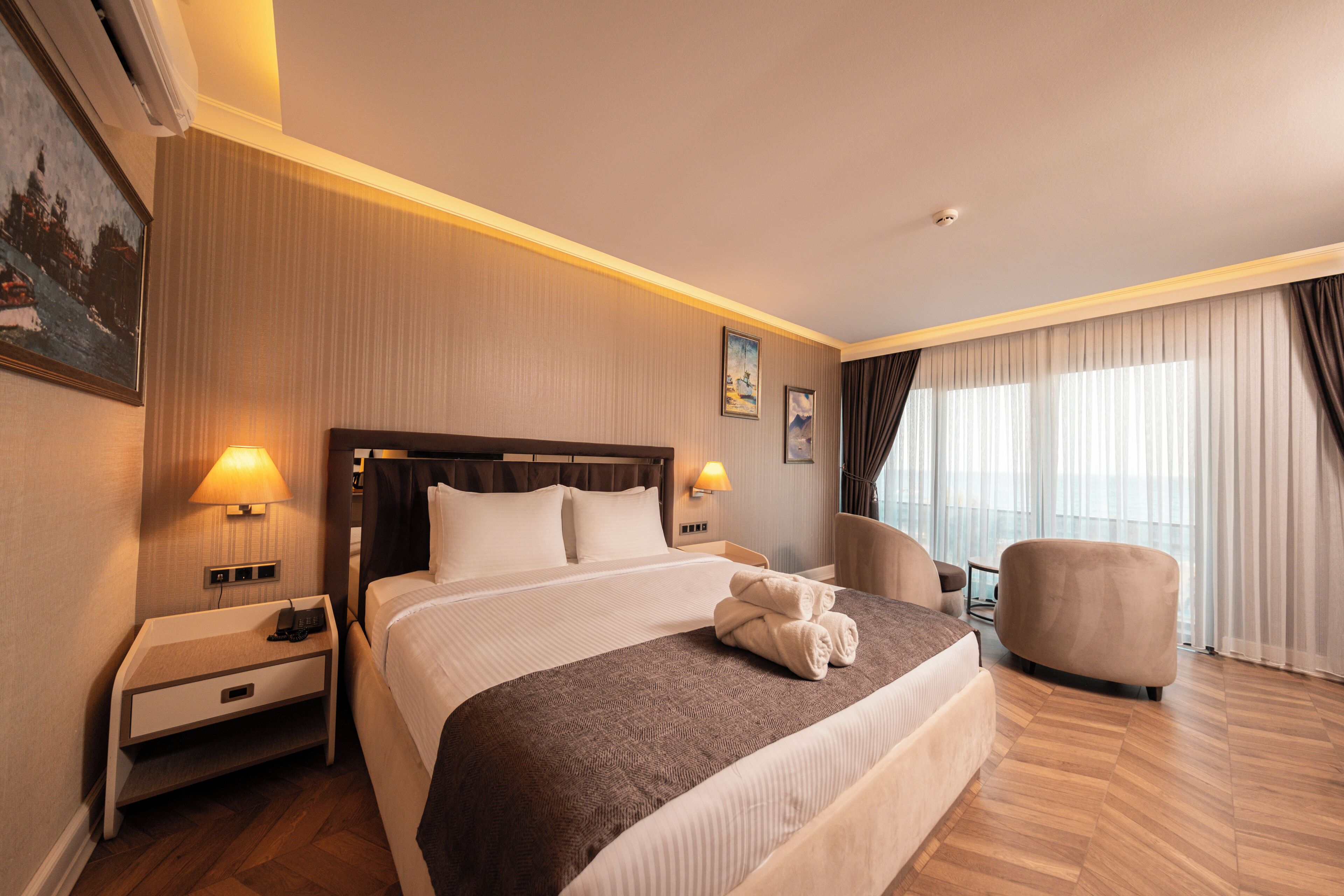 A hotel room with a large bed, bedside lamps, a nightstand, a chair, and a window with curtains.