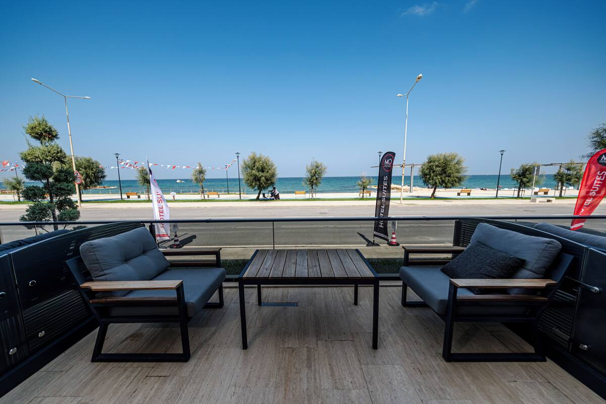Une terrasse avec deux canapés et une table, donnant sur une plage sous un ciel dégagé.