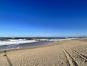 A beach with a clear sky, waves, and footprints in the sand.