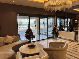 Un moderno vestíbulo de hotel con un amplio ventanal que ofrece vistas a la playa y árboles de Navidad decorados.