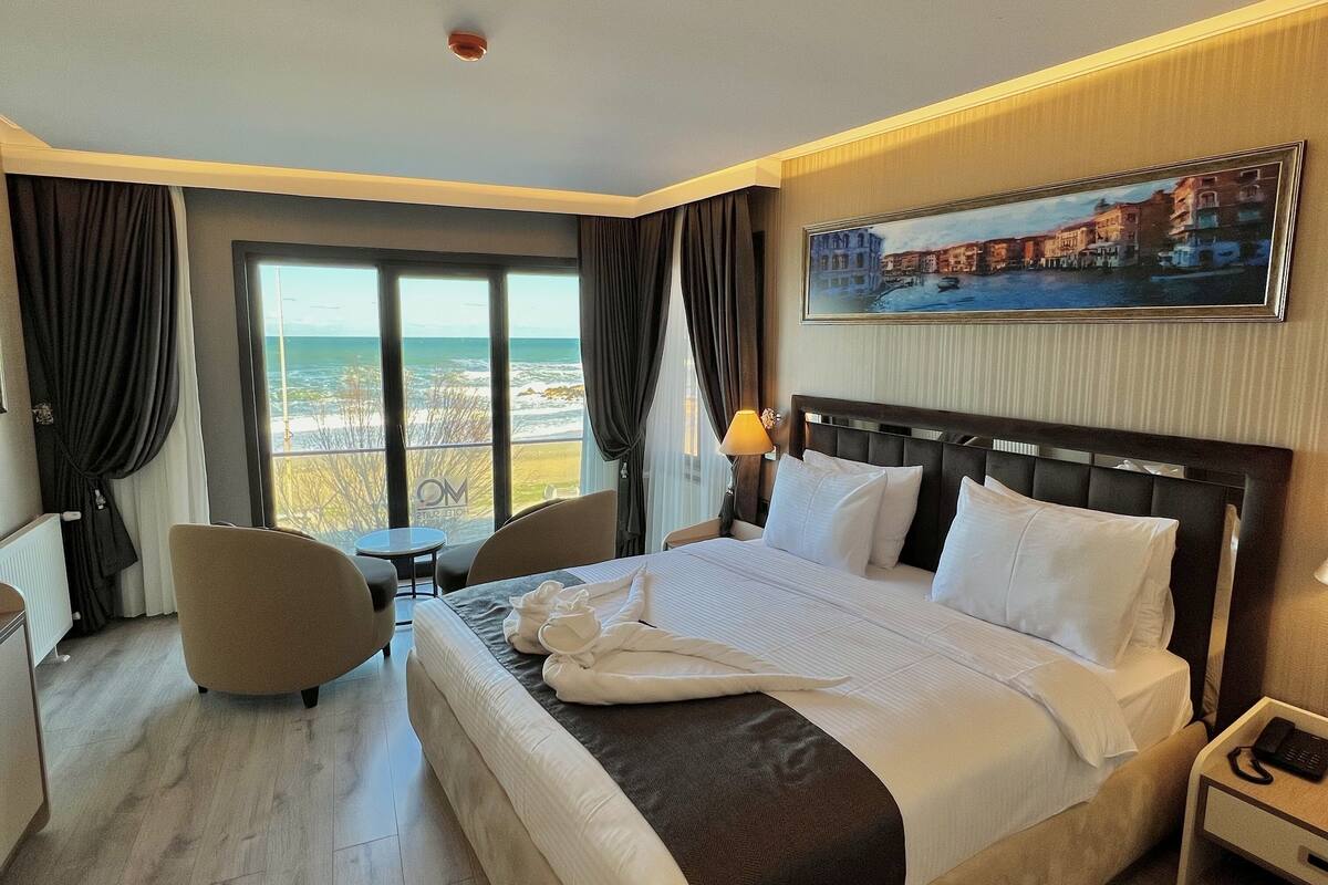 Une chambre d’hôtel avec un lit, un bureau, une chaise, une petite table et une vue sur la mer.